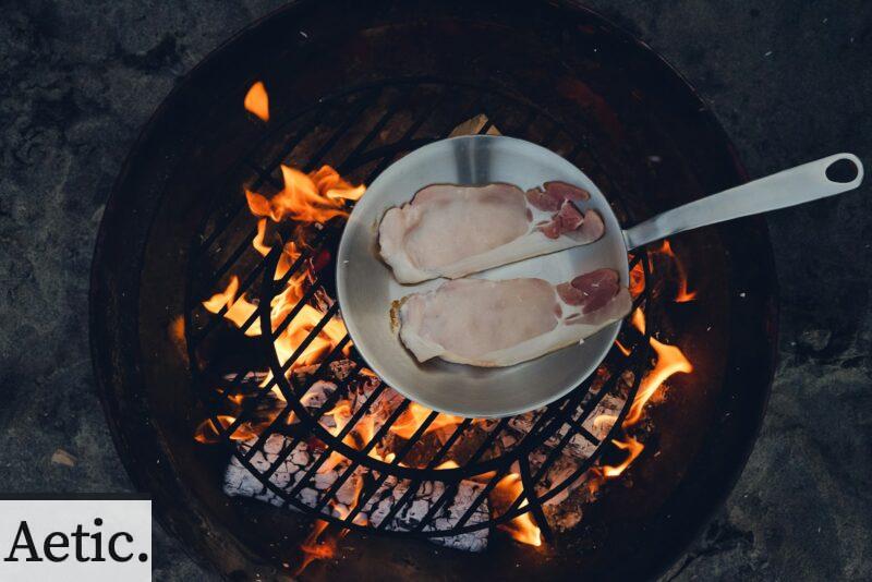 person cooking steak on charcoal gril