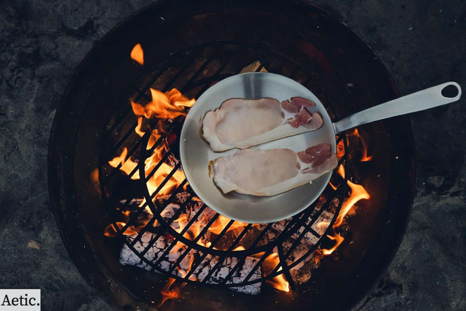 person cooking steak on charcoal gril