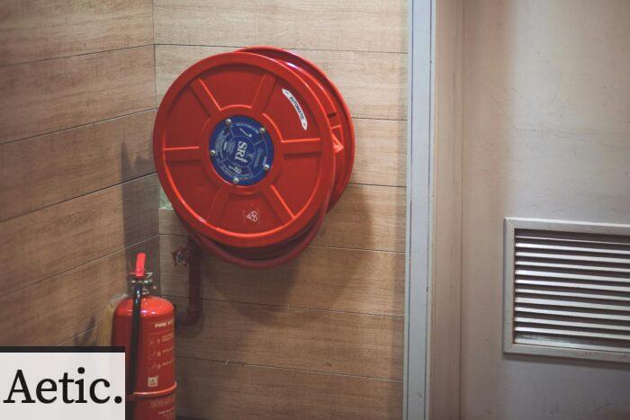 Red fire hose reel and extinguisher inside a building corner.