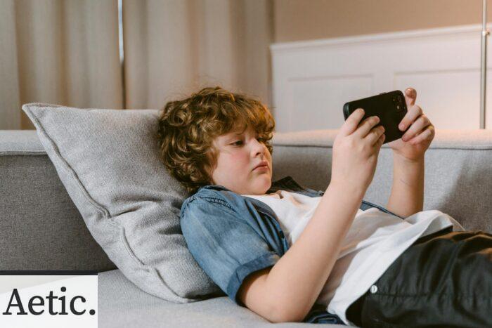 Young boy relaxing on a sofa, using a smartphone, indoors.