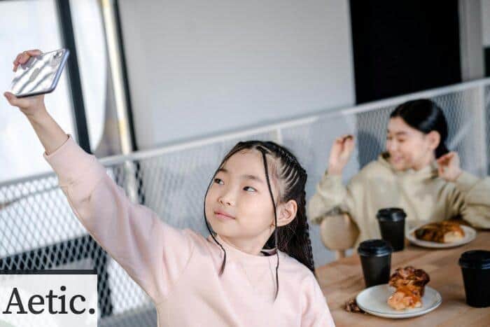 A young girl capturing a selfie indoors with a smartphone in a cozy cafe.